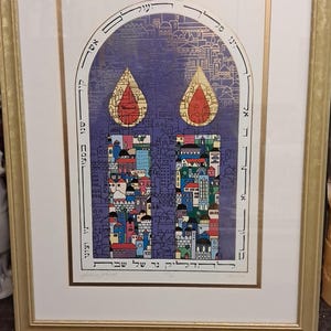 May include: Framed art print with a gold-colored frame. The artwork features a stylized depiction of a city with colorful buildings and two teardrop-shaped elements. Hebrew text is present in the design.