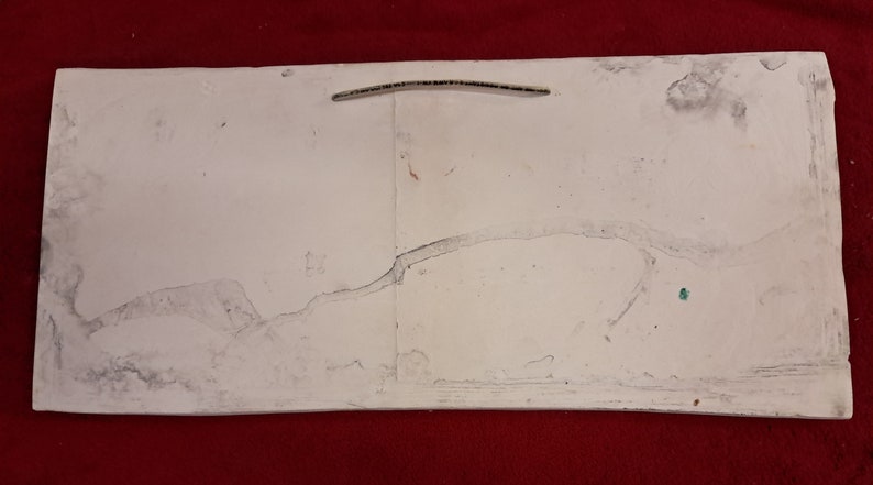 May include: A white, rectangular, ceramic tile with a crack running across the surface. The tile has a rough, textured surface and appears to be old and worn.