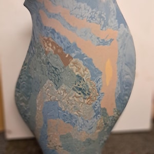 May include: A blue, beige, and brown ceramic vase with a textured surface. The vase has a unique, abstract design.