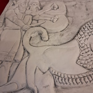 May include: A white plaster relief sculpture depicting three figures, possibly men, standing in front of a large, stylized animal. The figures are wearing long robes and have their arms raised. The animal has a scaly body and a large head with a wide mouth.