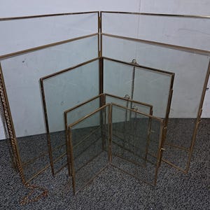 May include: Set of six gold-toned metal picture frames with glass panels. The frames are nested inside each other, with the largest frame at the back and the smallest frame at the front. Each frame has a hanging chain.