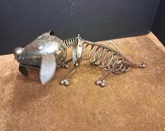 May include: A metal dog sculpture with a skeletal body and a detailed head. The dog's head is silver with a large, round nose and a detailed mouth. The body is made of springs and metal rods.