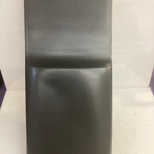 May include: A dark gray, rectangular, slightly curved, plastic panel with a smooth surface.