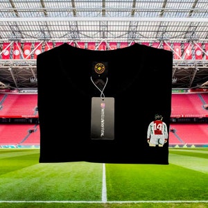 May include: Black t-shirt with a small embroidered image of a soccer player wearing a red and white jersey with the number 14 on the back. The t-shirt has a tag that says "TWOTYELLOWSOFFICIAL".