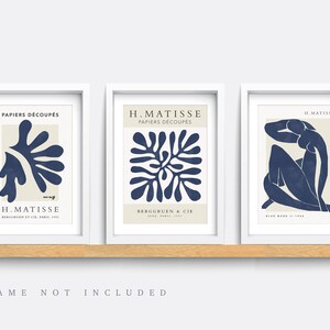 May include: Set of three blue and white art prints featuring abstract designs by Henri Matisse. The prints are titled "Papiers Decoupes" and feature a stylized plant, a geometric pattern, and a seated figure.