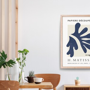 May include: A framed print of a blue abstract art piece by Henri Matisse. The print is titled "Papiers D&eacute;coup&eacute;s" and includes the artist's signature and the text "Berggruen et Cie, Paris, 1953".