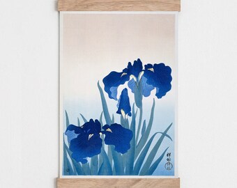 May include: A vintage Japanese woodblock print featuring three blue iris flowers with green leaves on a light blue and beige background. The print is framed with a natural wood frame.