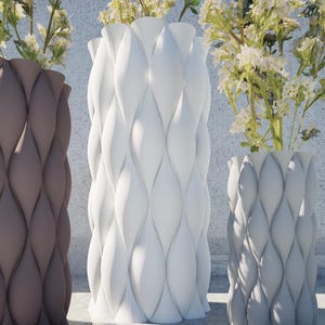Könnte beinhalten: Drei Vasen mit einem einzigartigen, strukturierten, pixelartigen Muster. Die Vasen sind braun, weiß und grau. Die Vasen sind mit weißen Blumen gefüllt.