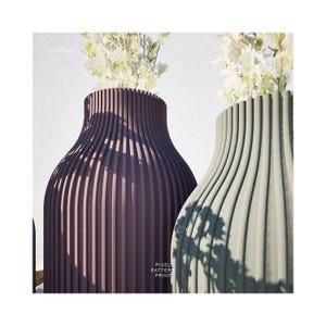 May include: Two ceramic vases with a ribbed design. The vase on the left is a deep purple color and the vase on the right is a light green color. Both vases have white flowers inside.