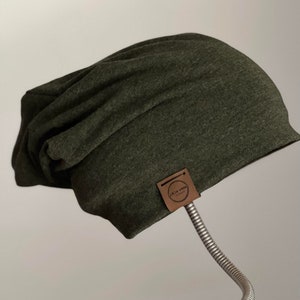 Peut inclure: Un bonnet mou en vert foncé avec une étiquette en cuir marron qui dit "Le Lab Store" en lettres blanches.