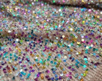 May include: Close-up of a shimmering fabric covered in iridescent sequins. The sequins are in various colors, including pink, blue, green, and purple, creating a sparkling effect. The fabric has a textured, ribbed appearance.