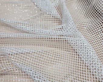 May include: Close-up of a white, sheer fabric with a grid-like pattern. The fabric is slightly crumpled, creating shadows and highlights. Small, reflective sequins are scattered across the surface, adding a subtle sparkle. The background is a soft, neutral tone.