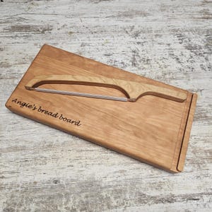 May include: A wooden bread board and bread knife set. The rectangular board is light brown with the text "Angie's bread board" engraved on the surface. The bread knife has a wooden handle and a stainless steel blade.