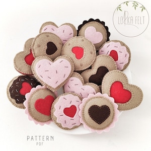 Peut inclure: Une collection de biscuits en forme de cœur en feutre de différentes couleurs et motifs, notamment rose, rouge, marron et blanc. Les biscuits sont disposés sur une assiette blanche. Le texte "PATTERN PDF" est visible en bas de l'image.
