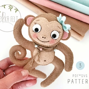 May include: A brown felt monkey toy with a blue bow, big eyes, and a curled tail. The monkey is wearing a beaded necklace and is holding a piece of twine. The toy is on a white background with a stack of felt fabric in the background. The text "PDF.SVG PATTERN" is on the bottom right of the image.