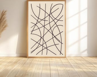 May include: Abstract art print in a wooden frame. The artwork features a cream-colored background with intersecting black lines. The frame is a light brown color. The print is displayed on a wooden floor against a white wall.