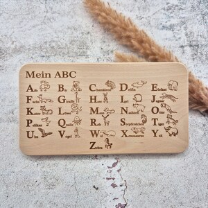 Könnte beinhalten: Holz-ABC-Tafel mit gravierten Buchstaben und Tierillustrationen. Auf der Tafel steht oben "Mein ABC". Jeder Buchstabe ist mit einem Tier gepaart, wie z. B. ein Bär für "B" und eine Giraffe für "G".