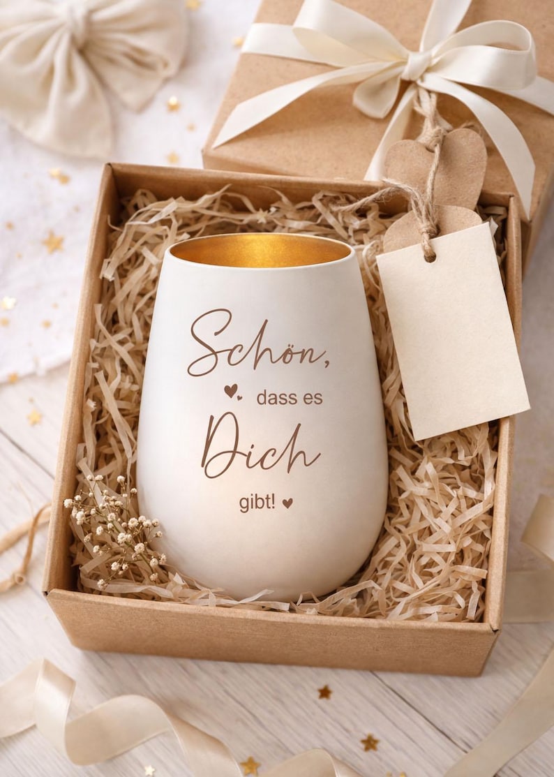 May include: A white, egg-shaped candle holder with gold interior, inscribed with the words "Sch&ouml;n, dass es Dich gibt!" in brown script. It rests in a brown box with shredded paper, a gift box, and a blank tag.