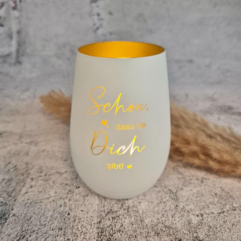 May include: A white, frosted glass with a gold rim. The glass has gold script that reads "Schon, dass es Dich gibt!" with a heart symbol. The glass is likely a candle holder or decorative item.