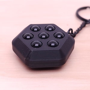 May include: A black hexagonal keychain with a textured surface and eight black rubber balls.