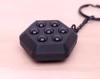 May include: A black hexagonal keychain with a textured surface and eight black rubber balls.