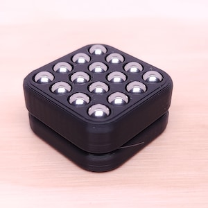 May include: A black, square-shaped object with a grid of 16 shiny, silver metal balls. The object is made of two stacked, identical pieces. The design is modern and geometric, with a focus on the contrast between the black and silver.