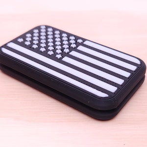 May include: A black and white American flag design printed on a black silicone case. The case is folded in half.