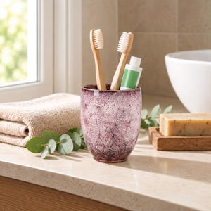 Pode incluir: Um copo cil&iacute;ndrico de cer&acirc;mica com acabamento esmaltado salpicado em roxo e branco. O copo cont&eacute;m duas escovas de dentes de bambu com cerdas brancas e um pequeno tubo de pasta de dentes branco com um r&oacute;tulo verde liso na parte frontal.