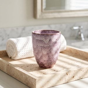 Pode incluir: Um copo cil&iacute;ndrico de cer&acirc;mica com um esmalte salpicado em tons de roxo profundo e branco. O recipiente tem uma forma lisa e ligeiramente c&oacute;nica com um acabamento texturado e irregular que cobre toda a sua superf&iacute;cie exterior.