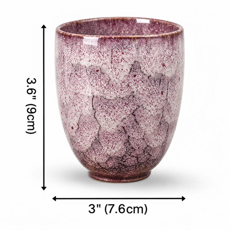 Pode incluir: Uma ch&aacute;vena de ch&aacute; em cer&acirc;mica com um acabamento de esmalte craquelado salpicado em roxo e branco. A ch&aacute;vena mede 9 cm de altura e 7,6 cm de di&acirc;metro. Apresenta um corpo arredondado que afunila para uma pequena base circular texturizada.