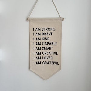 May include: A beige canvas banner with black text that reads "I am strong, I am brave, I am kind, I am capable, I am smart, I am creative, I am loved, I am grateful".