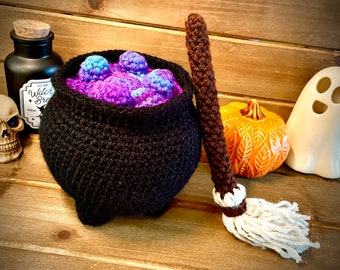Può includere: Un calderone in crochet nero pieno di palline viola e blu, una scopa in crochet marrone, un fantasma in ceramica bianca e una piccola bottiglia di vetro con un tappo di sughero e il testo "Witch Brew Potion" su una superficie di legno.