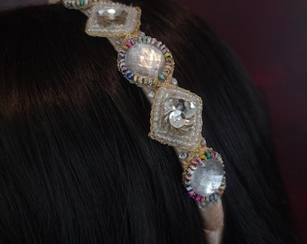 May include: A gold headband with a row of clear rhinestones and colorful beads. The headband is on a person's head.