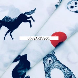 May include: White fabric with a repeating pattern of black unicorns, owls, bears, rabbits, and red circles. The text "JOSYARTSYCO." is printed on the fabric. The fabric is folded, showing multiple layers.