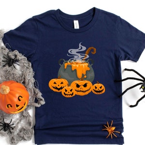 May include: A navy blue t-shirt with a graphic of a cauldron with orange pumpkin faces and a steaming orange liquid. The text "Boo!" is printed on the shirt.