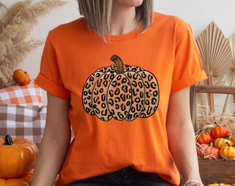 May include: A woman wearing an orange t-shirt with a black and brown leopard print pumpkin design. The shirt is a casual style with short sleeves and a crew neck.