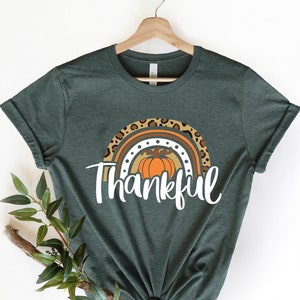 May include: A dark green t-shirt with a rainbow design featuring a pumpkin and the word "Thankful".