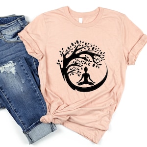 May include: A peach-colored t-shirt with a black graphic of a person meditating under a tree. The tree is stylized with a circular shape and leaves.