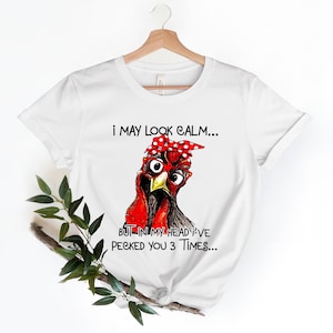 May include: White t-shirt with a cartoon illustration of a chicken wearing red and white polka dot bandana and glasses. The text on the shirt reads "I may look calm... But in my head I've pecked you 3 times..."