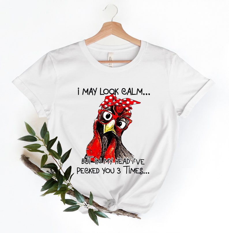 May include: White t-shirt with a cartoon illustration of a chicken wearing red and white polka dot bandana and glasses. The text on the shirt reads "I may look calm... But in my head I've pecked you 3 times..."