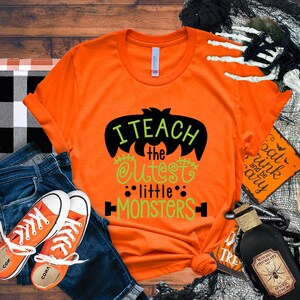 May include: Orange t-shirt with a black bat graphic and green text that reads "I teach the cutest little monsters".