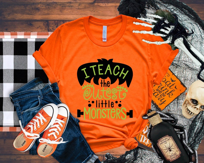 May include: Orange t-shirt with a black bat graphic and green text that reads "I teach the cutest little monsters".