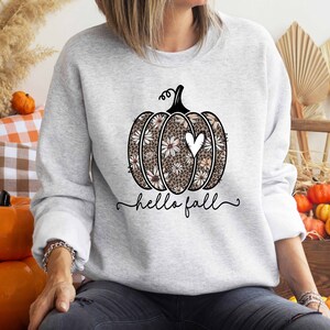 Puede incluir: Una sudadera gris con un dise&ntilde;o de calabaza floral y el texto "hello fall".