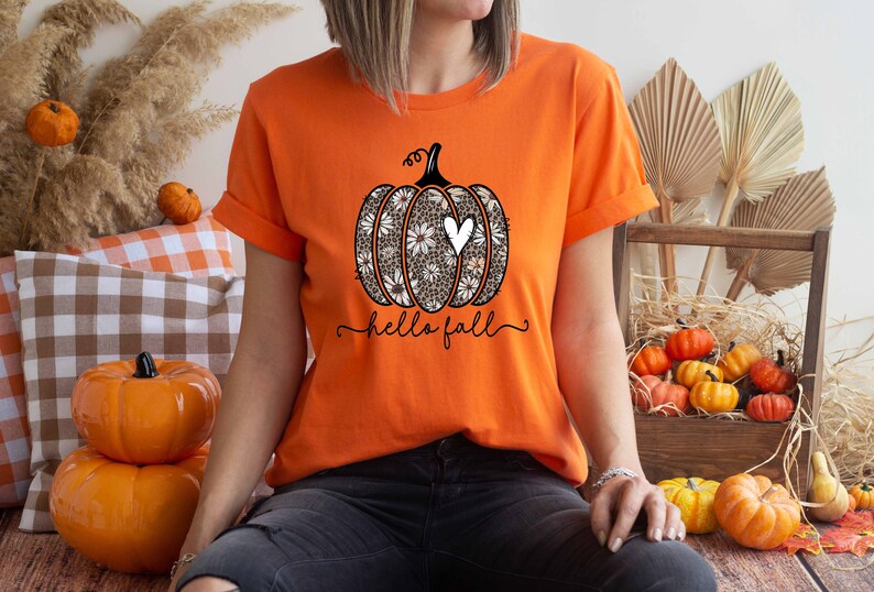 Puede incluir: Camiseta naranja con un gr&aacute;fico de una calabaza con un coraz&oacute;n blanco y el texto "hello fall".