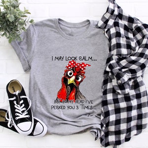 May include: Gray t-shirt with a red and white illustration of a chicken wearing a red bandana. The text on the shirt reads "I may look calm... But in my head I've pecked you 3 times..."