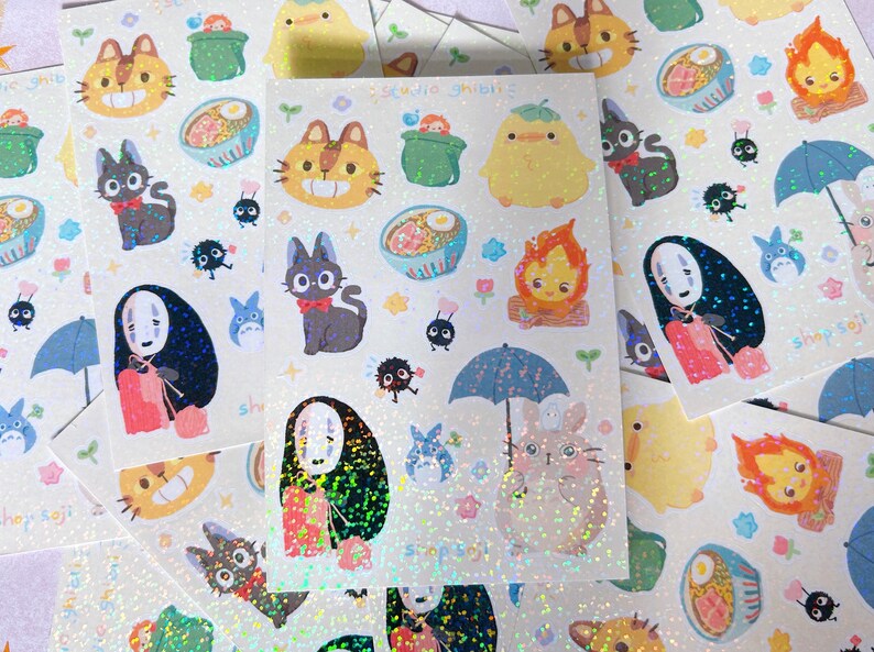 May include: Sheets of holographic stickers featuring Studio Ghibli characters. Designs include cats, soot sprites, Totoro, and characters from Spirited Away. The stickers have a glittery, iridescent finish and the text "shopsoji" is visible.