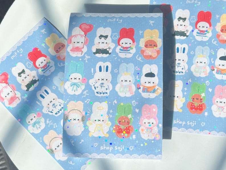 May include: Sheets of stickers featuring cartoon bunnies in various outfits and poses. The stickers are on a light blue background with the word "miffy" at the top and "shop soji" at the bottom. The stickers have a glittery effect.
