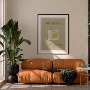 May include: A framed print with the text "GIN & TONIC" hangs above a brown leather sofa. The print features a graphic of a cocktail with a lemon slice. A large potted plant and a small side table complete the room.