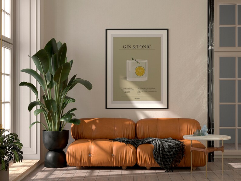 May include: A framed print with the text "GIN & TONIC" hangs above a brown leather sofa. The print features a graphic of a cocktail with a lemon slice. A large potted plant and a small side table complete the room.
