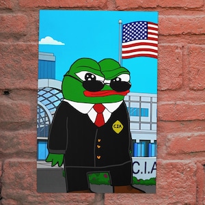 Könnte beinhalten: Gerahmter Cartoon-Druck mit einem grünen Frosch in einem schwarzen Anzug, Sonnenbrille und roter Krawatte. Der Frosch steht vor einem Gebäude mit einer amerikanischen Flagge und "C.I.A.". Der Hintergrund ist ein blauer Himmel.